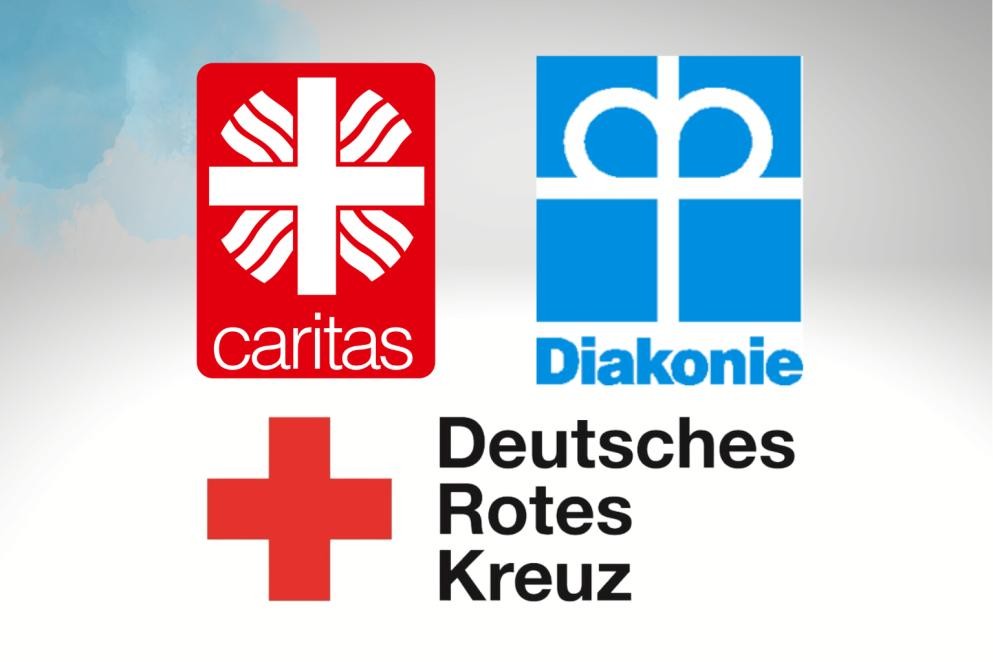 Das Foto zeigt das rot-weiße Logo der Caritas, das blau-weiße Logo der Diakonie und das rot-schwarze Logo des Deutschen Roten Kreuzes.